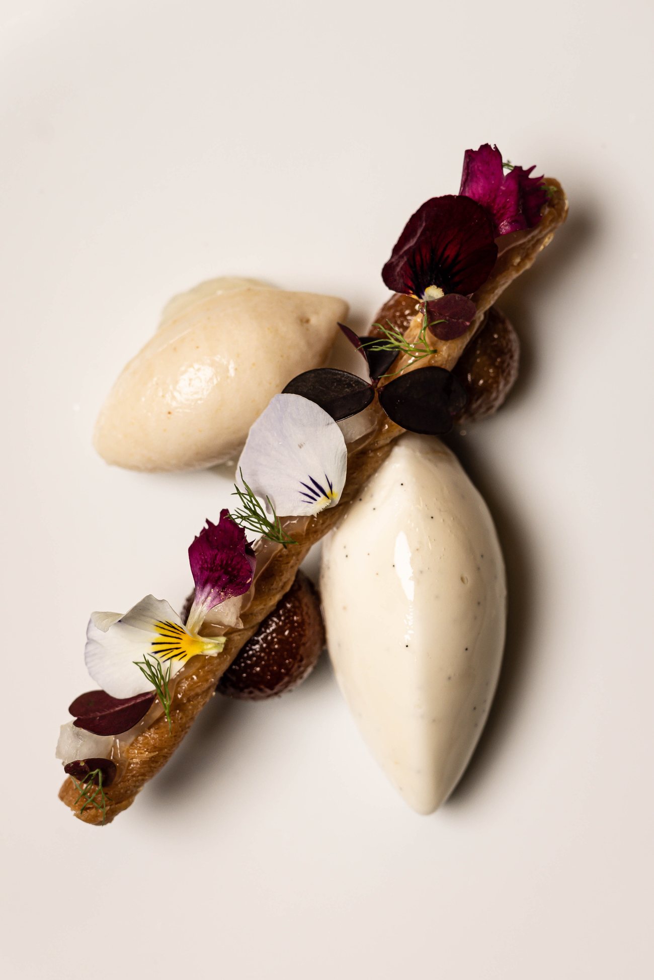 Un dessert de Substance : quenelles glacées, pétales et sablé, sur assiette blanche