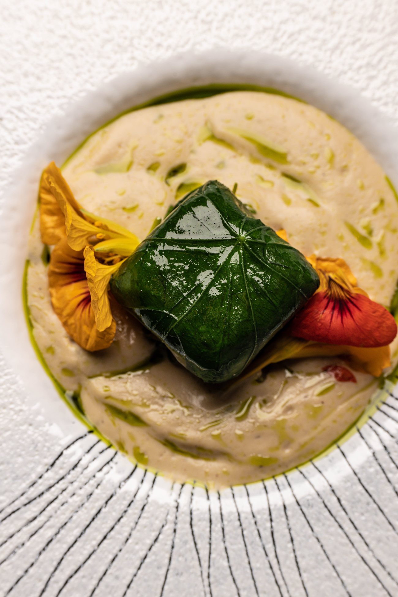 Une assiette de Substance : feuille verte, fleurs et crème sur porcelaine rayée